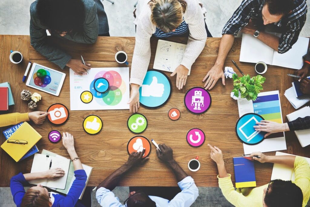 A group of people sitting around a table that has social media icons on the table.